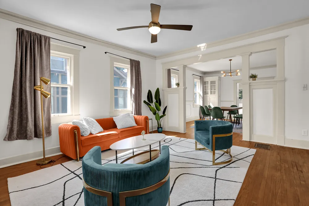 The living room with an orange sofa, teal velvet chairs and a neon Memphis sign.